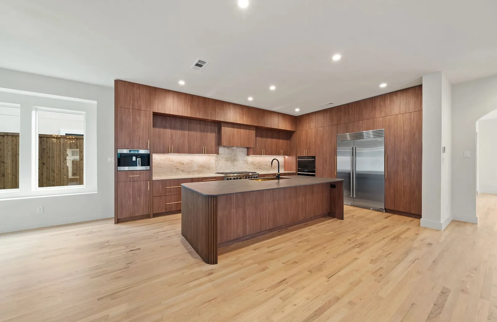 Walnut kitchen with a fluted island, stone backsplash and integrated refrigerator