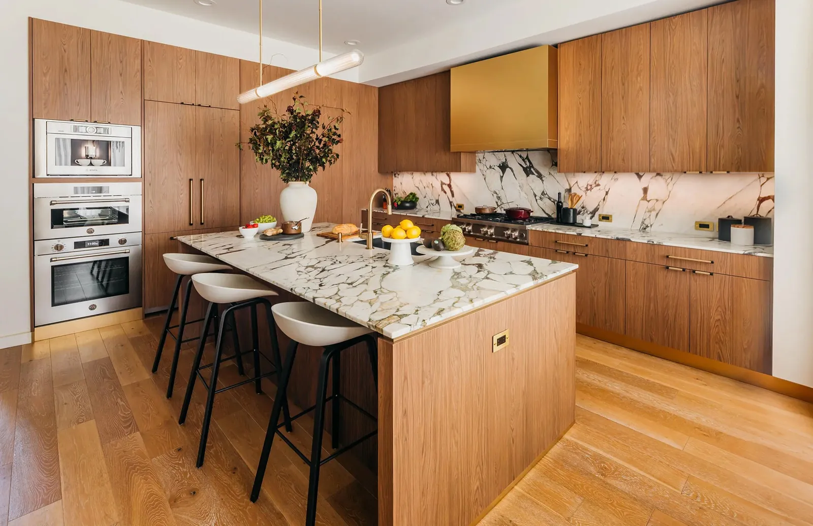 Walnut kitchen with a marble island, brass hood and white bar stools