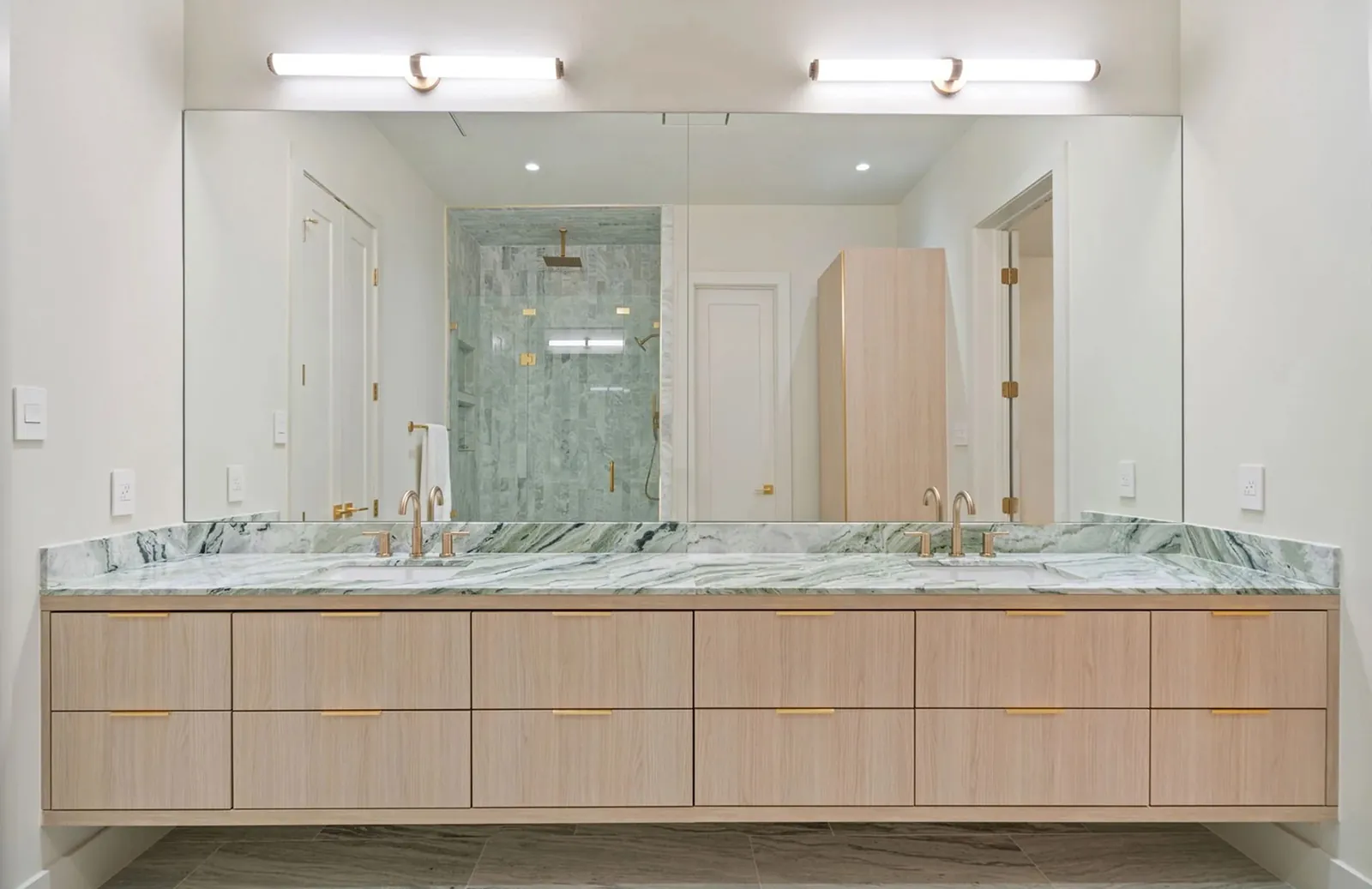 Floating oak double vanity with a green marble top and brass fixtures